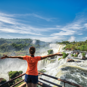 Mulher de braços abertos e ao fundo as cataratas do Iguaçu