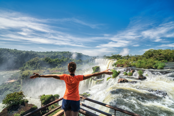 Mulher de braços abertos e ao fundo as cataratas do Iguaçu