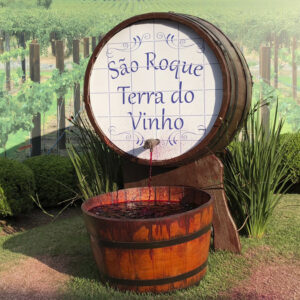 Imagem de um barril, saindo vinho por uma torneira. No barril se lê "São Roque - Terra do Vinho"