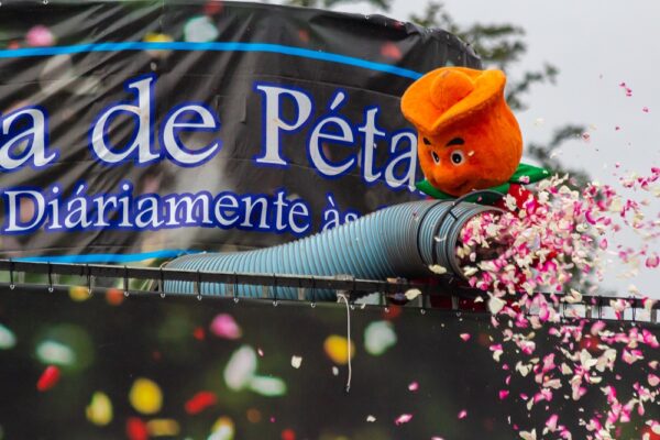 Mascote da Expoflora segurando uma mangueira por onde sai pétalas de rosas